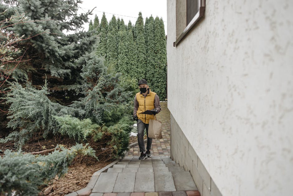 A delivery person wearing a mask walks along a path outdoors carrying a bag.